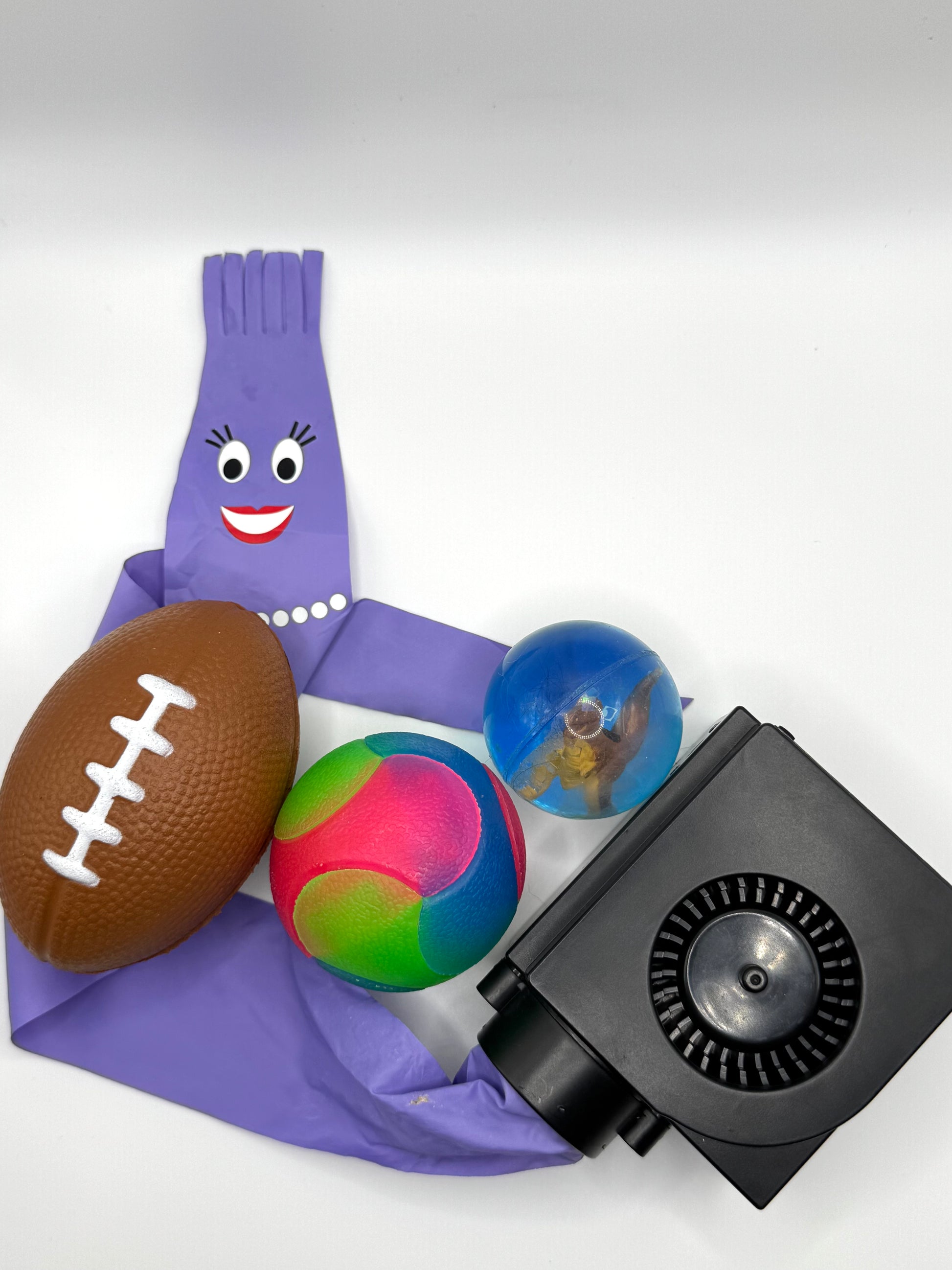 Purple toy with various items including a football, colorful ball, and black device on a white background