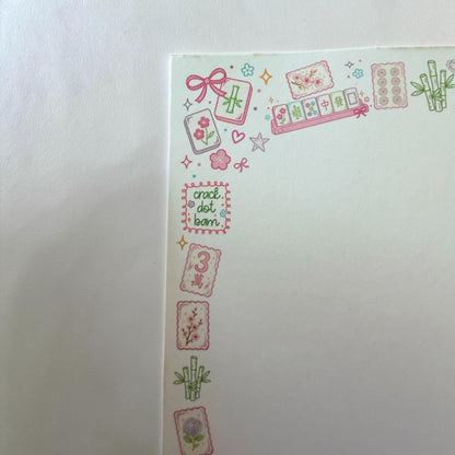 A close-up of a white paper corner decorated with pink and green Japanese mahjong-themed washi tape stickers, including tiles, bamboo, stars, and the text 'crack dot bam'.